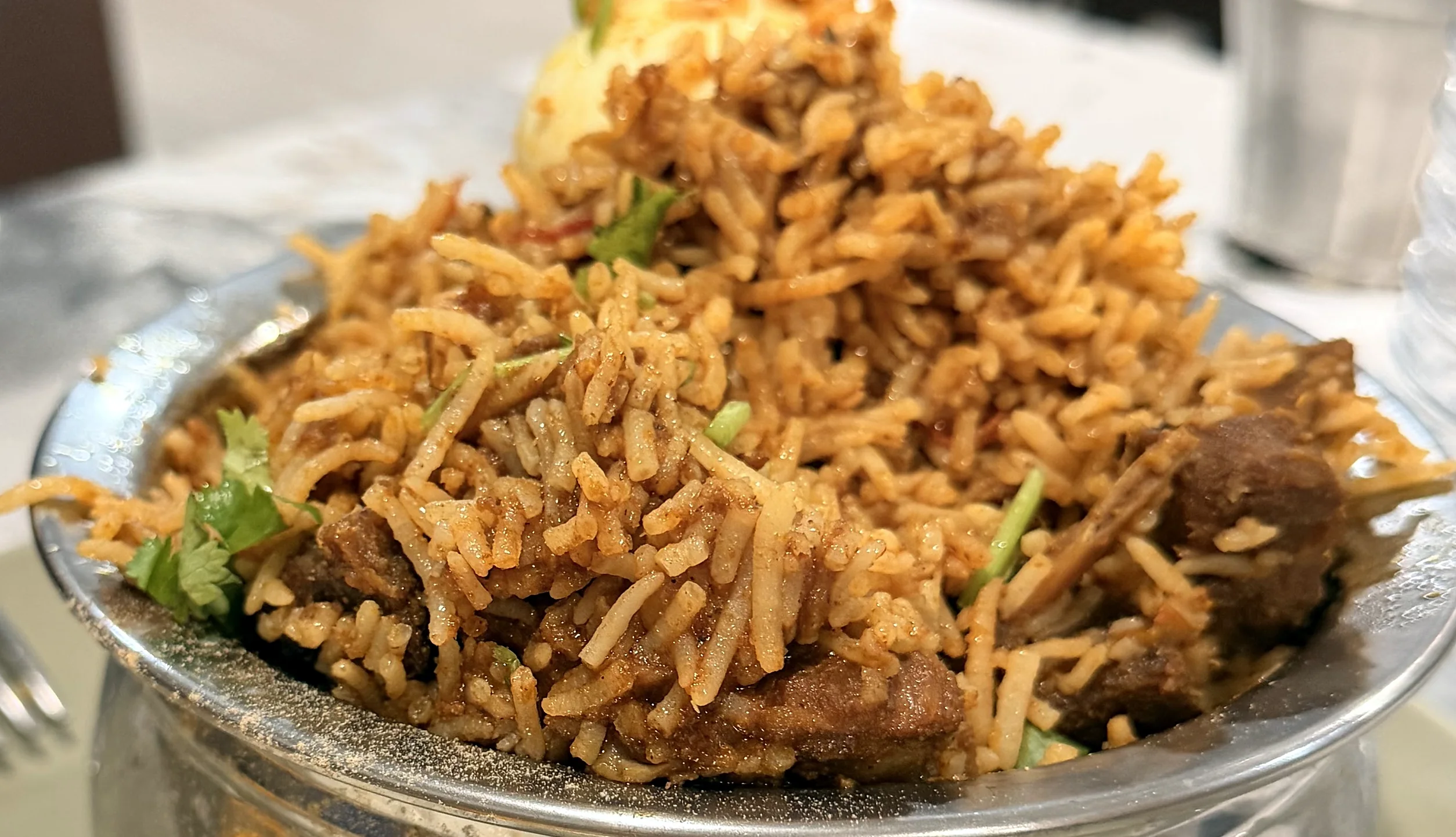 Close-up of biryani with meat pieces and coriander in a steel bowl