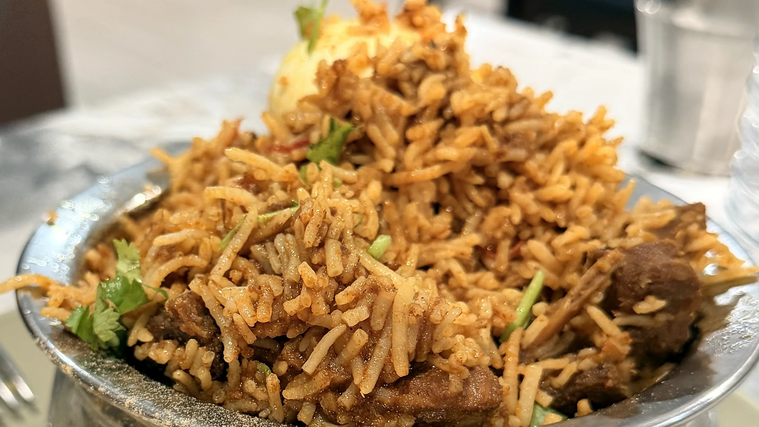 Biryani with meat pieces and coriander in a steel bowl