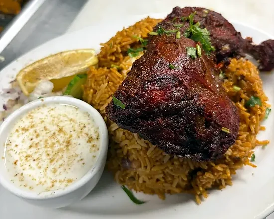 Chicken biryani with a roasted chicken leg, raita, lemon and onion